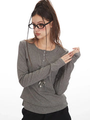 Close-up of a woman wearing a grey long-sleeved shirt, black cargo pants, and a star pendant necklace, posing with her hands.