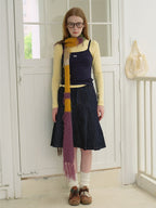 Full body shot of a woman standing in front of a white door, wearing a long striped scarf.