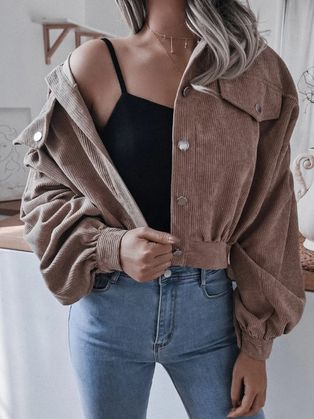 Woman wearing a brown corduroy cropped jacket with balloon sleeves and a black crop top, jacket open.