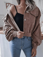 Woman wearing a brown corduroy cropped jacket with balloon sleeves and a black crop top, jacket open.
