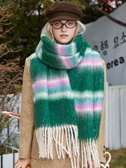 Model wearing a tan coat and a green plaid scarf with cream, pink, and blue stripes. She is also wearing a brown flat cap and round glasses.