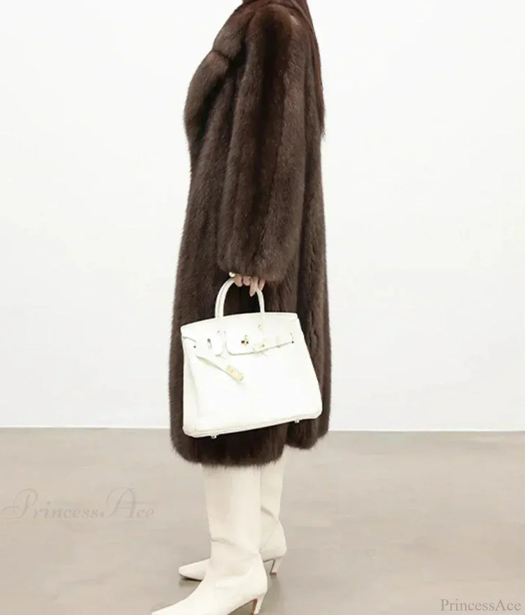 Side view of a woman in a brown mink fur coat, holding a white handbag.