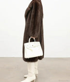 Side view of a woman in a brown mink fur coat, holding a white handbag.