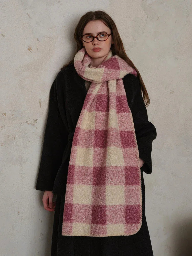 Woman wearing a black coat and a pink and cream plaid scarf.