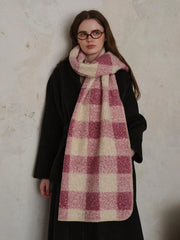 Woman wearing a black coat and a pink and cream plaid scarf.