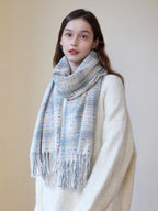 A young woman models a cozy white sweater and a plaid scarf with fringe detail.