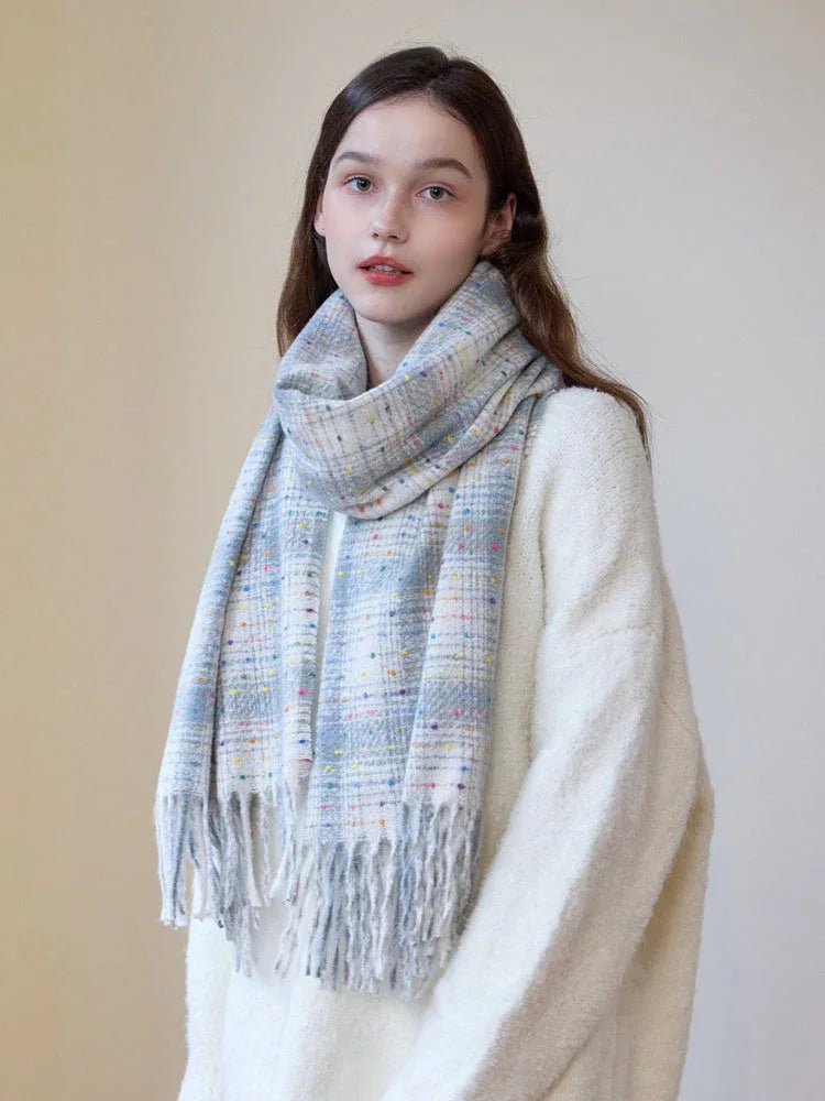 A young woman models a cozy white sweater and a plaid scarf with fringe detail.