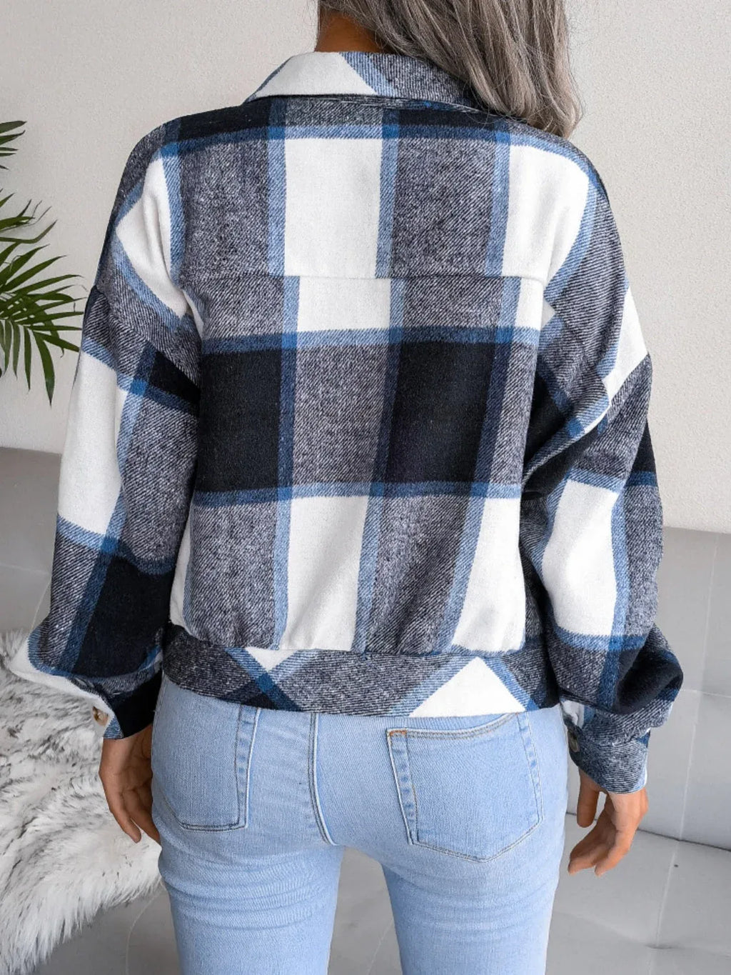 Back view of a woman wearing a blue, white, and black plaid flannel shirt jacket over light wash jeans.