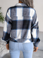 Back view of a woman wearing a blue, white, and black plaid flannel shirt jacket over light wash jeans.