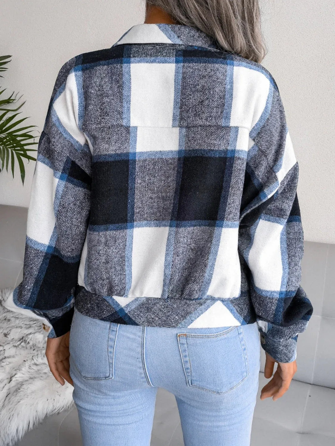 Back view of a woman wearing a blue, white, and black plaid flannel shirt jacket over light wash jeans.