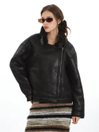 Model wearing a black faux leather jacket with shearling lining and sunglasses, adjusting the collar.
