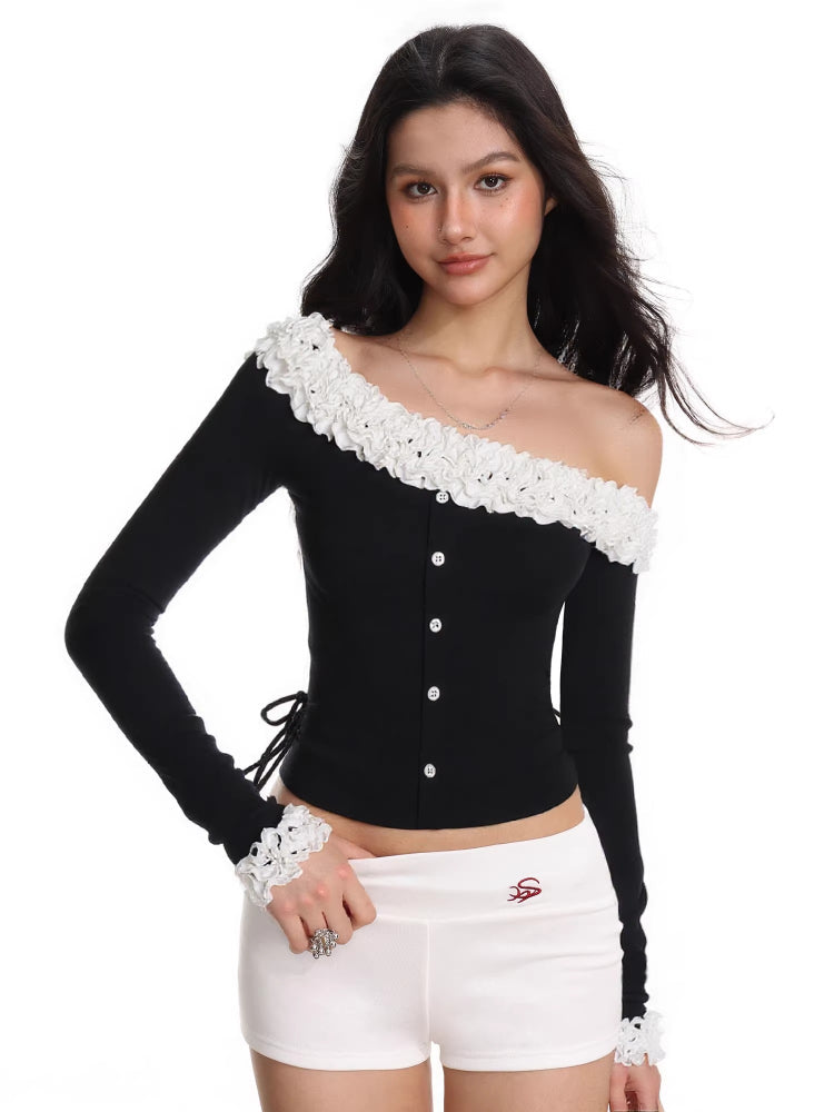 Model wearing a black off-the-shoulder long-sleeved top with white ruffled trim and white shorts, with one shoulder exposed.