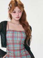 Close-up of a woman's face, winking, wearing a plaid mini dress and a sheer black cardigan.