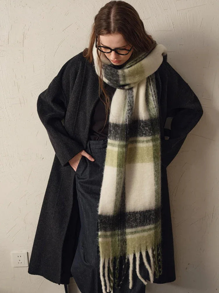 woman wearing a dark coat and a green and white plaid scarf, with one hand in her pocket
