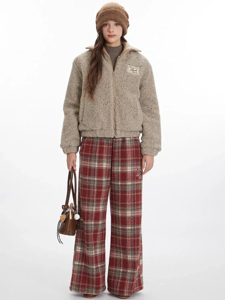 Model wearing a beige fuzzy bomber jacket with red plaid pants and a brown beanie, holding a brown handbag.