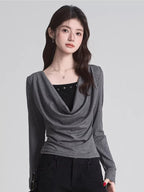 Woman wearing a grey draped long-sleeve top over a black camisole, paired with black pants.