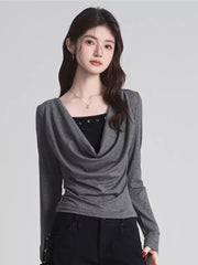 Woman wearing a grey draped long-sleeve top over a black camisole, paired with black pants.