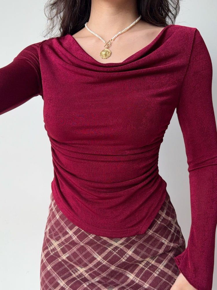Front view of a woman in a burgundy ruched cowl neck top and plaid skirt.