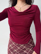 Front view of a woman in a burgundy ruched cowl neck top and plaid skirt.