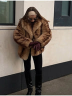 Woman wearing a tan and brown faux fur cropped jacket with black pants and burgundy gloves.