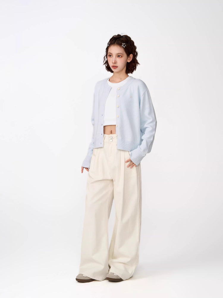 Full body shot of a woman in a light blue cropped knit cardigan, white crop top, and cream wide-leg pants, looking to the side.