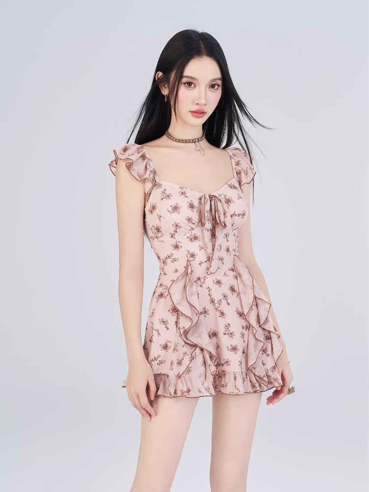 Full body shot of a woman in a pink floral print mini dress with flutter sleeves and ruffle trim.