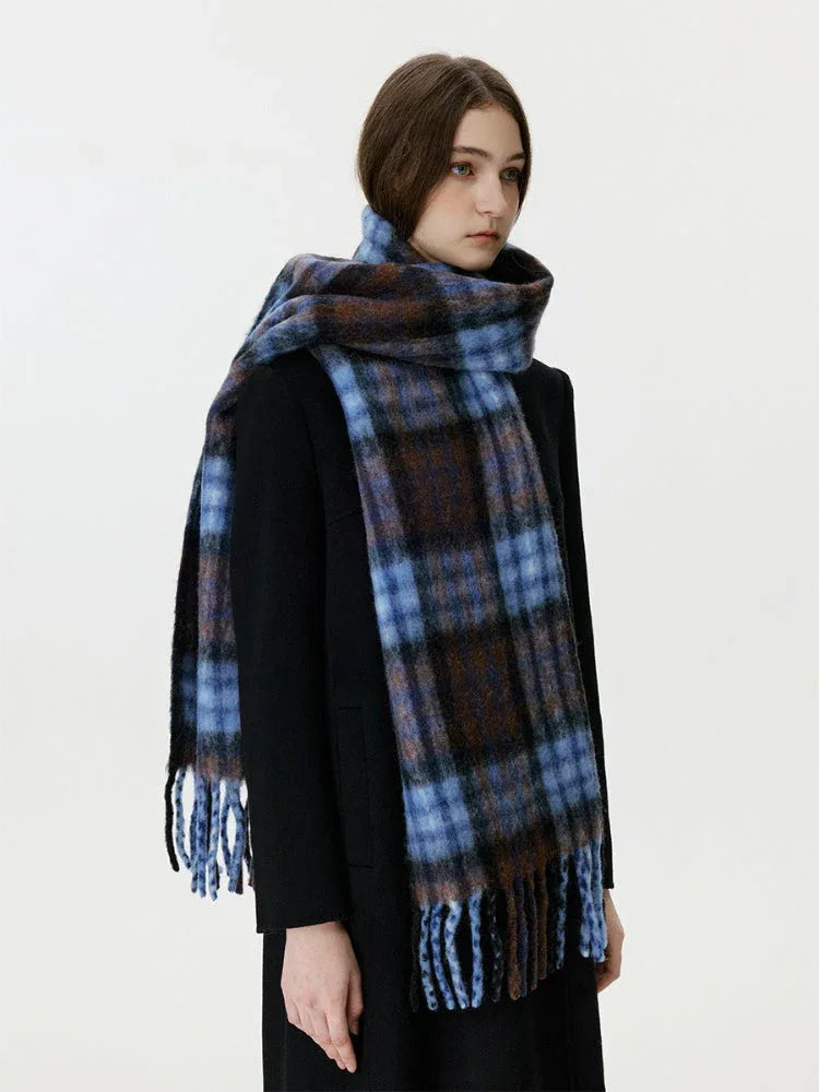Woman wearing a black coat and a blue and brown plaid scarf with fringe.