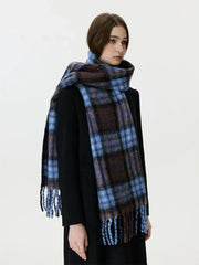 Woman wearing a black coat and a blue and brown plaid scarf with fringe.