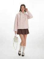 Full-body shot of a model in a pink quilted jacket, brown skirt, and white socks, holding a white handbag.