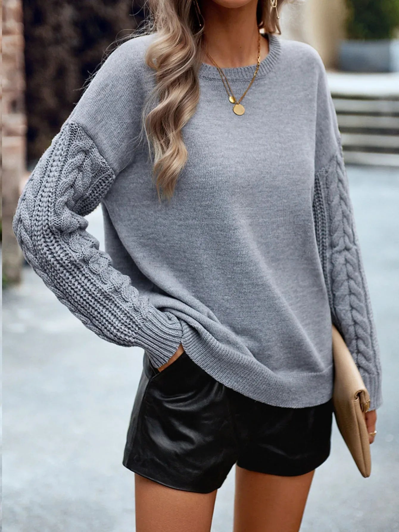 Close-up of a woman wearing a grey knit sweater with cable knit sleeves and black shorts.