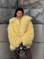 Woman wearing a yellow shaggy faux fur jacket with a black headband and a black handbag.