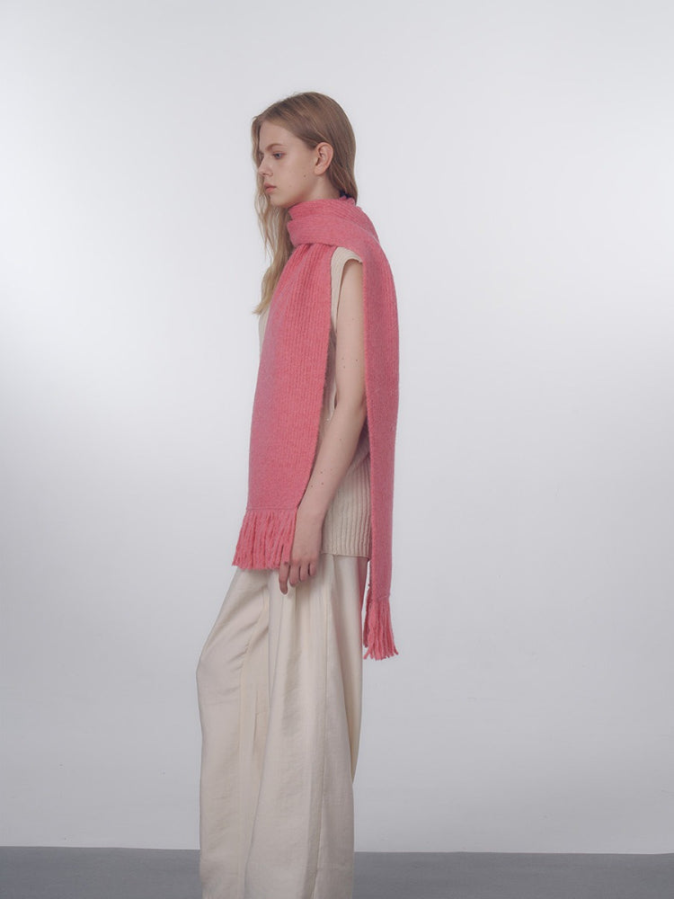 A model poses with a long pink knitted scarf wrapped around her neck and shoulders.