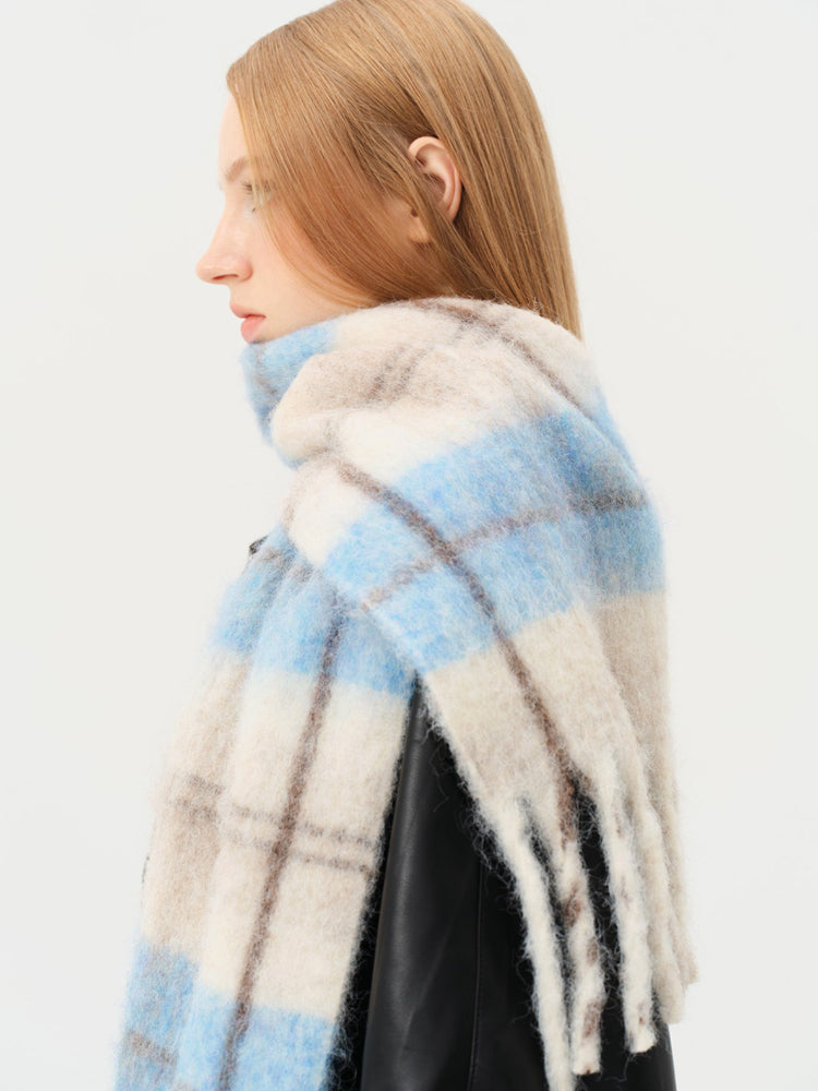 Close-up of a model wearing a fuzzy blue and beige plaid scarf with fringe