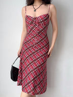 A woman wearing a red plaid midi dress with spaghetti straps and a tie-front bodice, holding a black handbag.