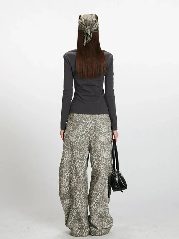 Back view of a woman wearing a dark grey long-sleeve top and wide-leg grey leopard print pants. She is holding a dark handbag and wearing a patterned headscarf.