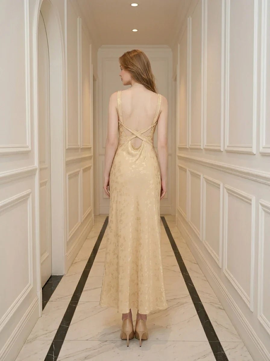 Back view of a woman wearing a sleeveless yellow maxi dress with a floral jacquard pattern and criss-cross back straps.
