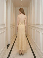 Back view of a woman wearing a sleeveless yellow maxi dress with a floral jacquard pattern and criss-cross back straps.