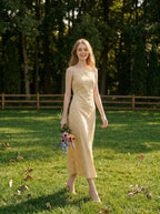 Woman wearing a sleeveless yellow maxi dress with a floral jacquard pattern walking in a grassy area with a bouquet of flowers.
