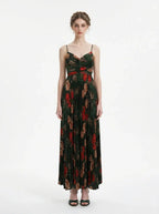 Woman wearing a dark green floral print maxi dress with spaghetti straps and a pleated skirt, front view.