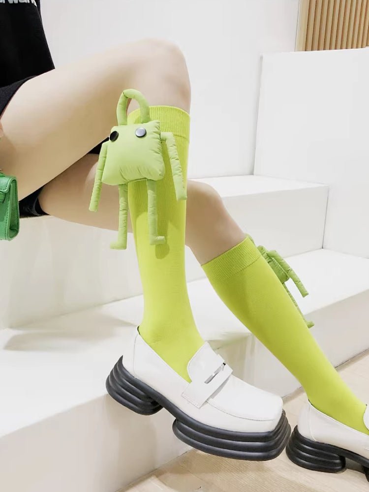 Close-up of a person's legs wearing bright green knee-high socks with a plush character accessory and white platform loafers.
