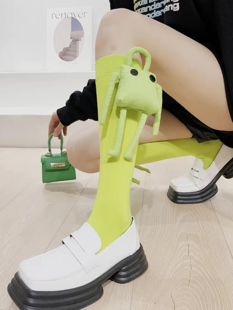 Side view of a person wearing bright green knee-high socks with a plush character and white platform loafers, holding a matching green mini handbag.