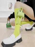 Side view of a person wearing bright green knee-high socks with a plush character and white platform loafers, holding a matching green mini handbag.