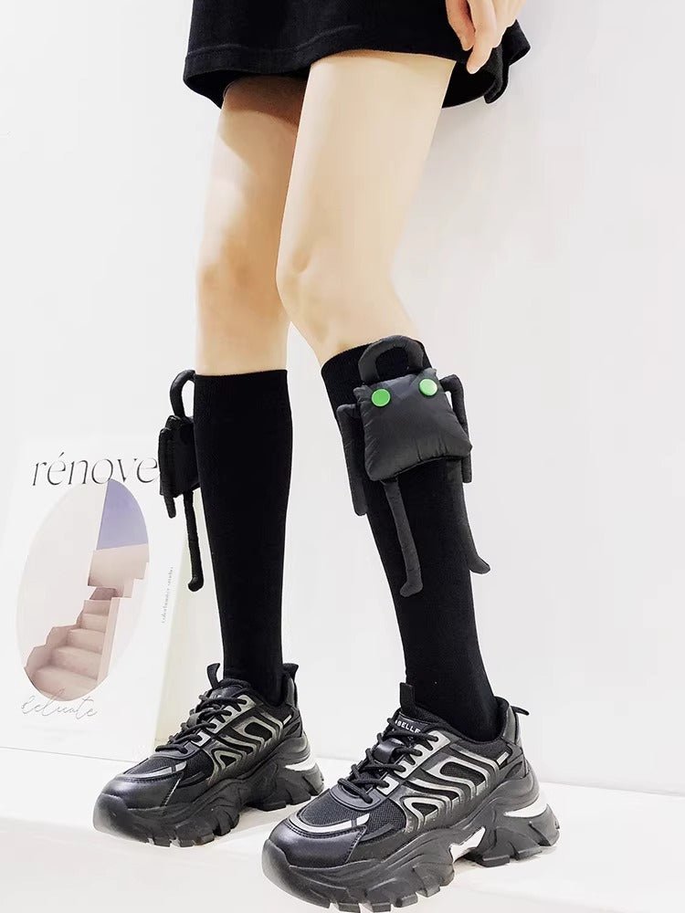 Person wearing black knee-high socks with a plush character accessory and black chunky sneakers.