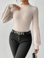 Woman wearing a cream-colored ribbed knit bodysuit with puff sleeves and a mock neck, accessorized with a black belt and gold rings.
