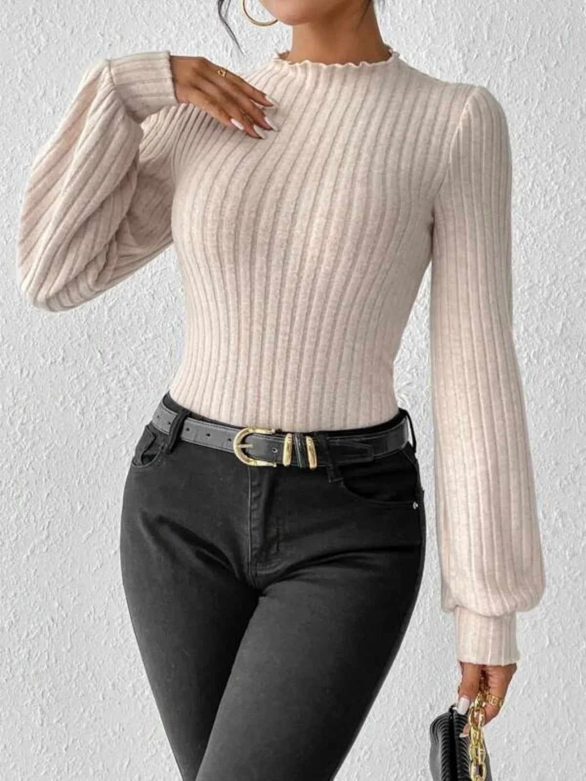 Woman wearing a cream-colored ribbed knit bodysuit with puff sleeves and a mock neck, accessorized with a black belt and gold rings.