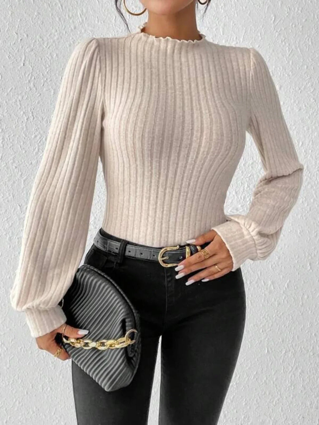 Woman holding a black clutch with a gold chain, wearing a cream-colored ribbed knit bodysuit with long puff sleeves and a mock neck.