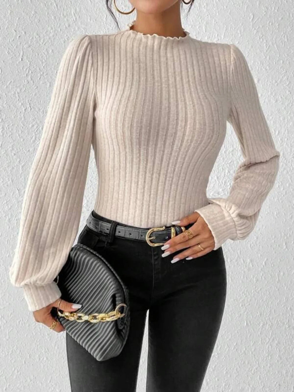 Woman holding a black clutch with a gold chain, wearing a cream-colored ribbed knit bodysuit with long puff sleeves and a mock neck.