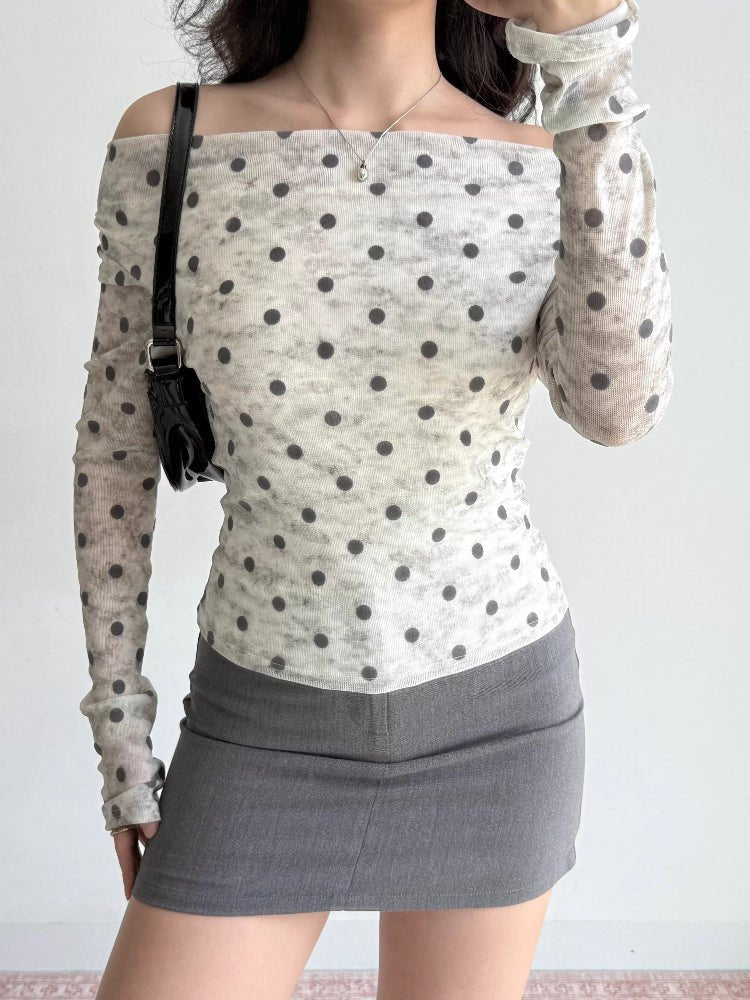 Woman wearing a white and grey polka dot off-the-shoulder mesh top and grey skirt, holding a black handbag