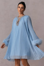 woman wearing a light blue pleated mini dress with feather cuffs and an embellished neckline