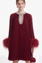 woman wearing a burgundy pleated mini dress with feather cuffs and an embellished neckline